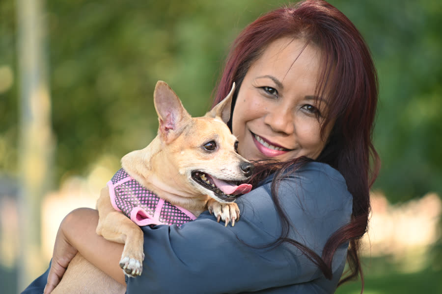 A woman holding her small dog close, both smiling