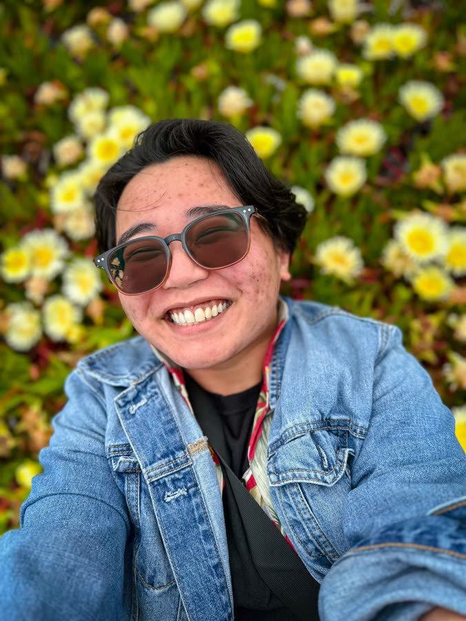 A smiling portrait in a denim jacket against flowering ice plant