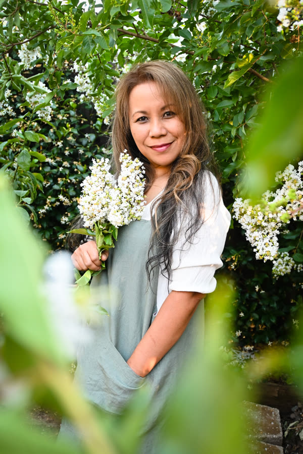 A woman holding white lilacs, framed by green leaves
