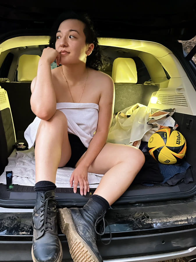 A person seated in an open car hatch in soft evening light